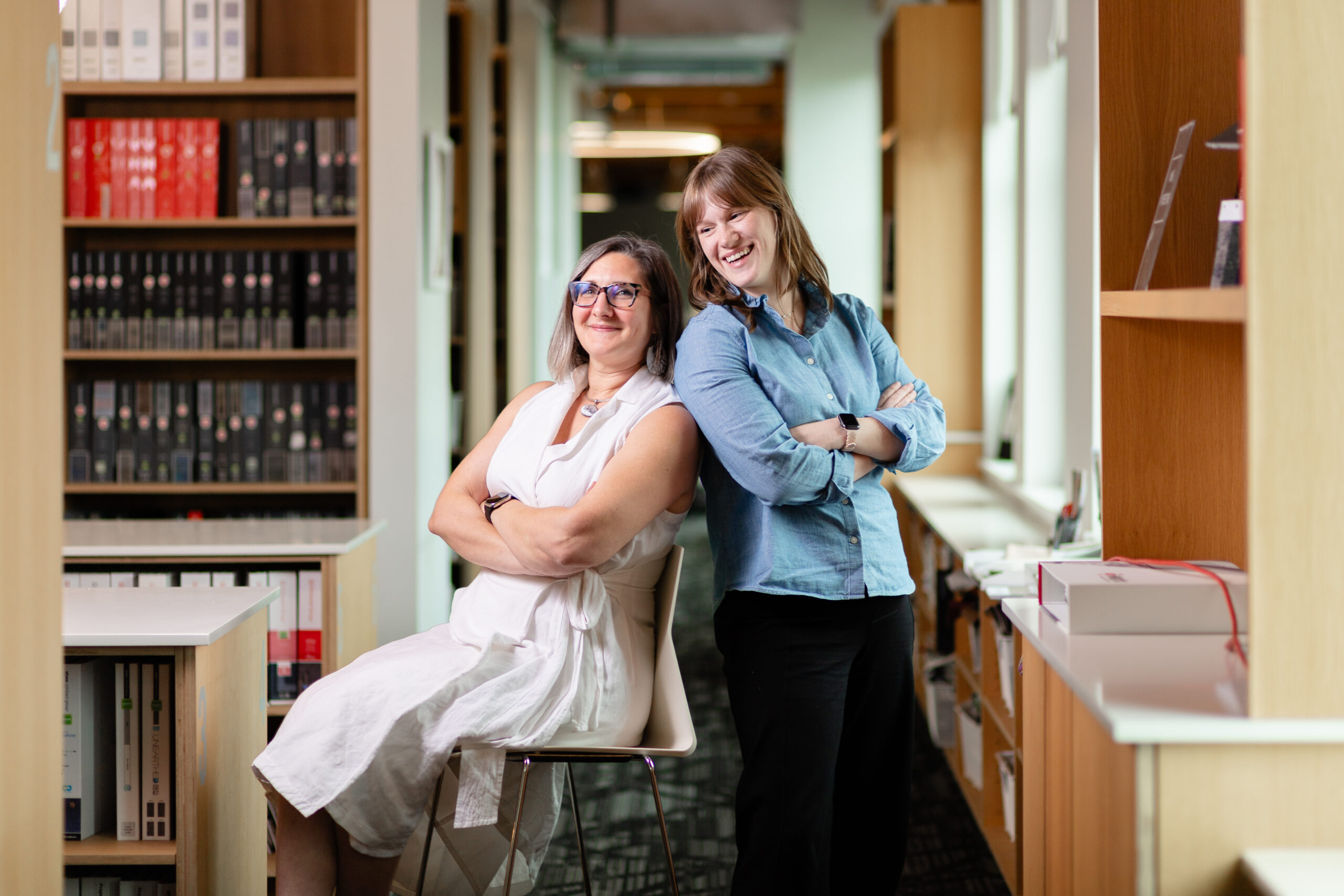 Ashlee Washington and Mariah Kiersey stand back-to-back with their arms crossed in the materials library of Ankrom Moisan's Portland office.